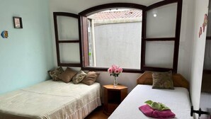 Een kamer met twee bedden, een kleine tafel met een bloemenvaas en een raam met uitzicht op een pannendak.
