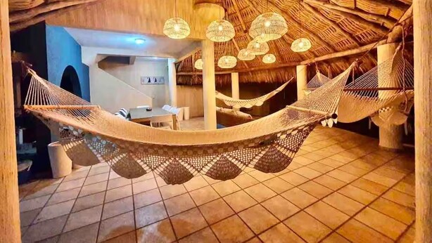 A hammock in a thatched-roof room with a small table and chairs.
