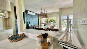 A modern kitchen with a marble countertop, a hanging light fixture, and a sailboat decoration.