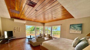 A spacious bedroom with a large bed, a TV, and a balcony with a view of the beach.