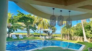 A pool area with a view of the ocean, surrounded by palm trees and lounge chairs.