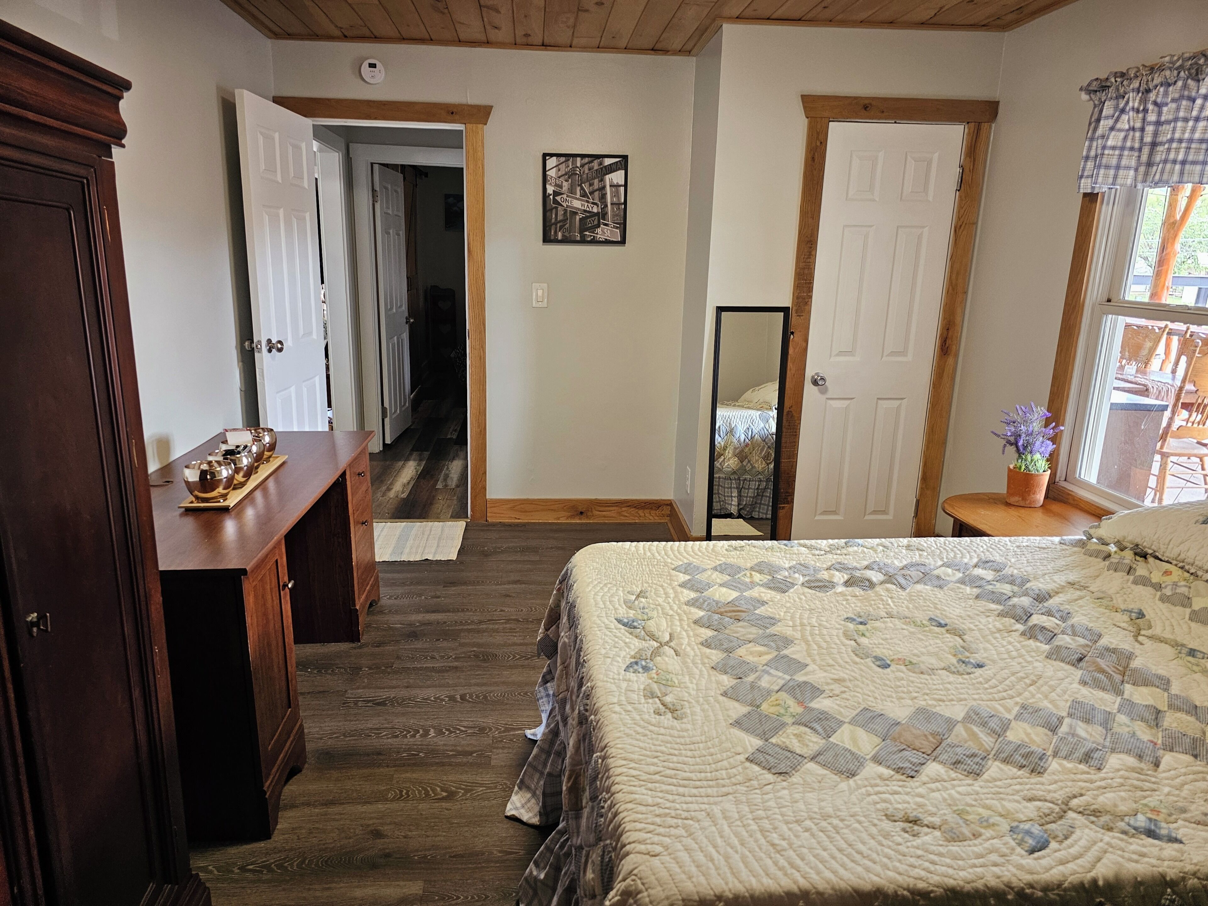 A bedroom with a bed, wooden dresser, and a hallway leading to another room.
