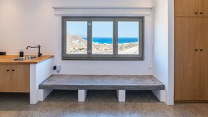 A kitchen with a built-in bench, a window with a view of the sea, and wooden cabinets.