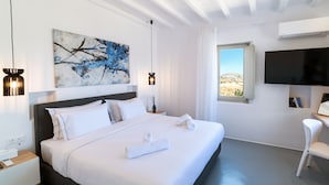 A modern hotel room with a large bed, a flat-screen TV, a painting, and a view of a desert landscape.