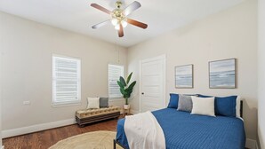A bedroom with a bed, a ceiling fan, a window with blinds, a door, and a plant. - Sleeps 10, Walk to the Beach and Pleasure Pier in Charming Historic Home (Galveston)