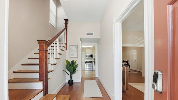 A hallway with wooden stairs, a potted plant, a rug, and a view into a kitchen area. - Sleeps 10, Walk to the Beach and Pleasure Pier in Charming Historic Home (Galveston)
