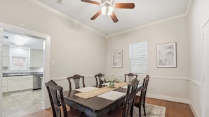 A dining area with a dark wooden table, six chairs, a ceiling fan, and artwork on the walls. - Sleeps 10, Walk to the Beach and Pleasure Pier in Charming Historic Home (Galveston)