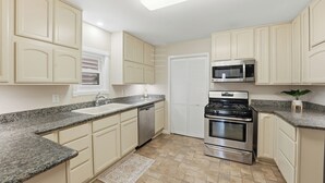 A kitchen with beige cabinets, granite countertops, a stainless steel stove, and a microwave. - Sleeps 10, Walk to the Beach and Pleasure Pier in Charming Historic Home (Galveston)