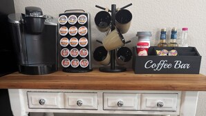 Una estación de café con cafetera Keurig, máquinas de café Dunkin' Donuts y Starbucks, un molinillo de café y un recipiente para guardar café.