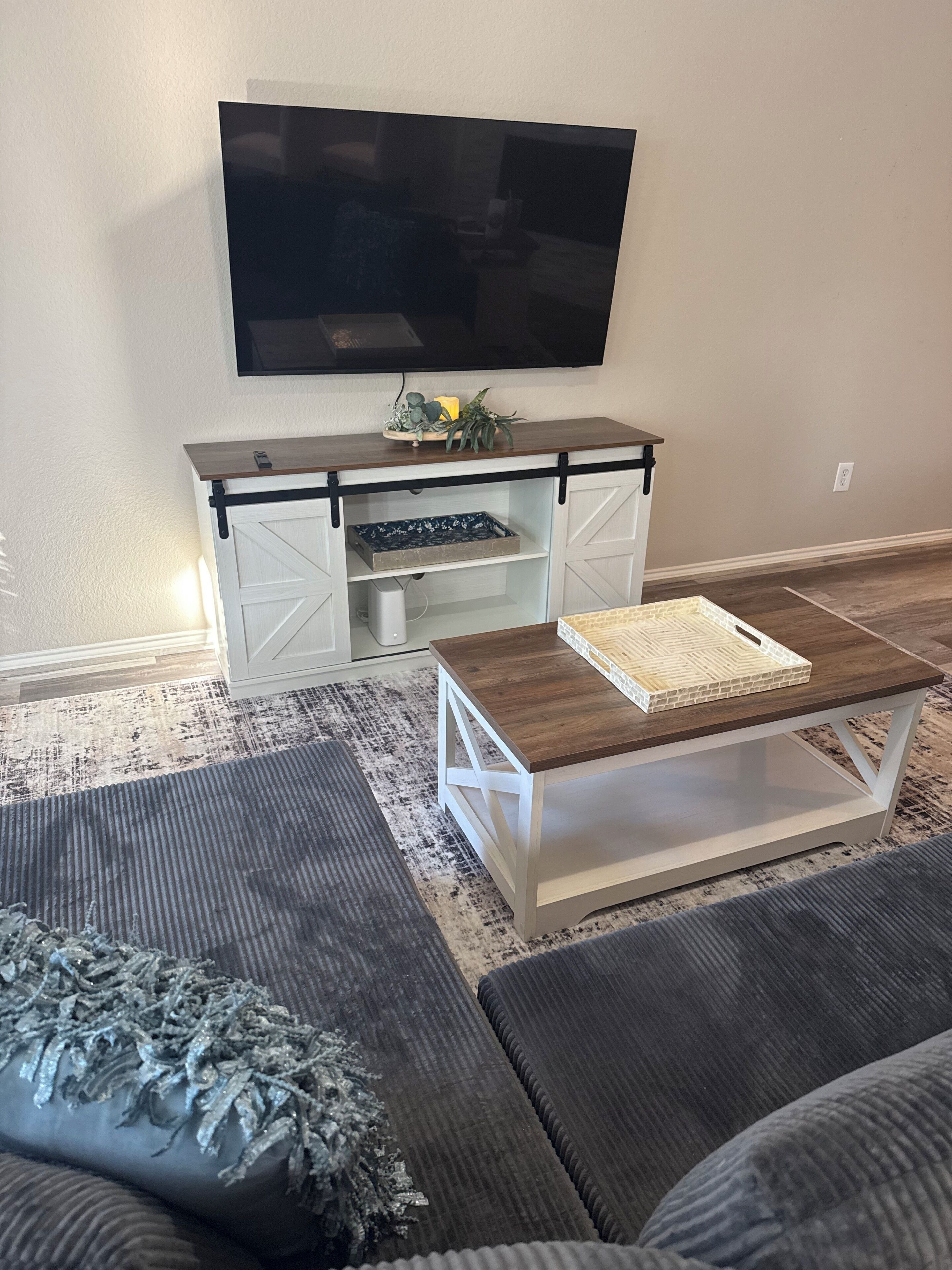 A living room with a flat-screen TV mounted on the wall, a wooden coffee table, a sofa, and a patterned rug.