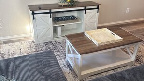 Una sala de estar con televisor de pantalla plana montado en la pared, una mesa de centro de madera, un sofá y un tapete estampado.