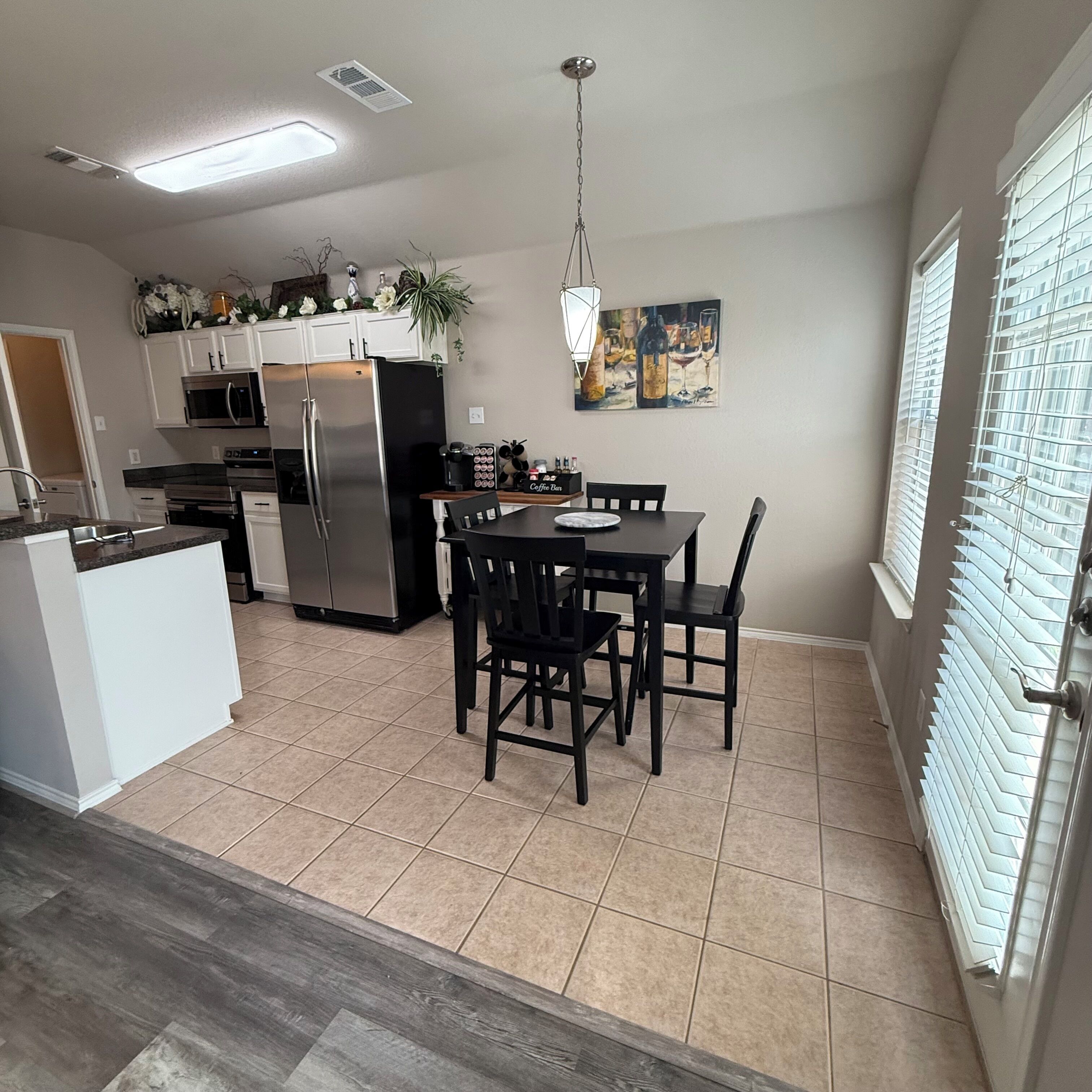 A modern kitchen with a dining area, stainless steel appliances, and a large window with blinds.