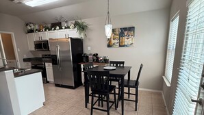 Una cocina moderna con comedor, electrodomésticos de acero inoxidable y un amplio ventanal con persianas.