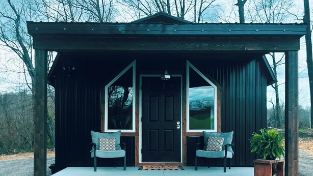 A wooden cabin with a porch, two chairs, a door, and a potted plant. - Kate’s Cottage
cozy 1-bedroom cottage nestled in the woods (Minford)