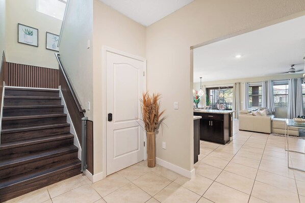 A modern interior with a staircase, a white door, and a living area with a sofa and dining table. - 6BR Themed Villa w/ Game Room+ Pool & Spa Solterra (Davenport)