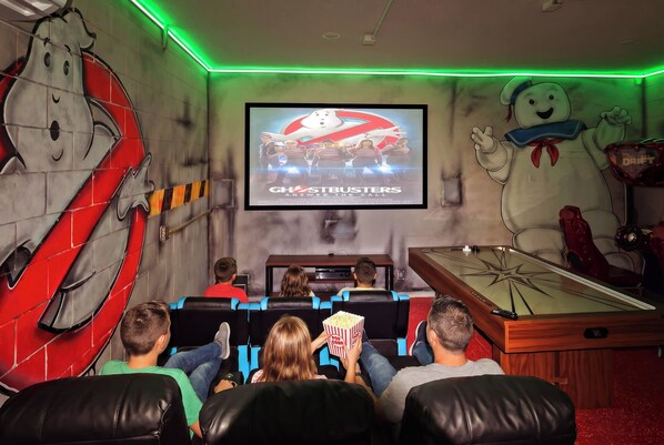 A movie theater with a Ghostbusters poster on the wall, a pool table, and people seated watching a film. - 6BR Themed Villa w/ Game Room+ Pool & Spa Solterra (Davenport)