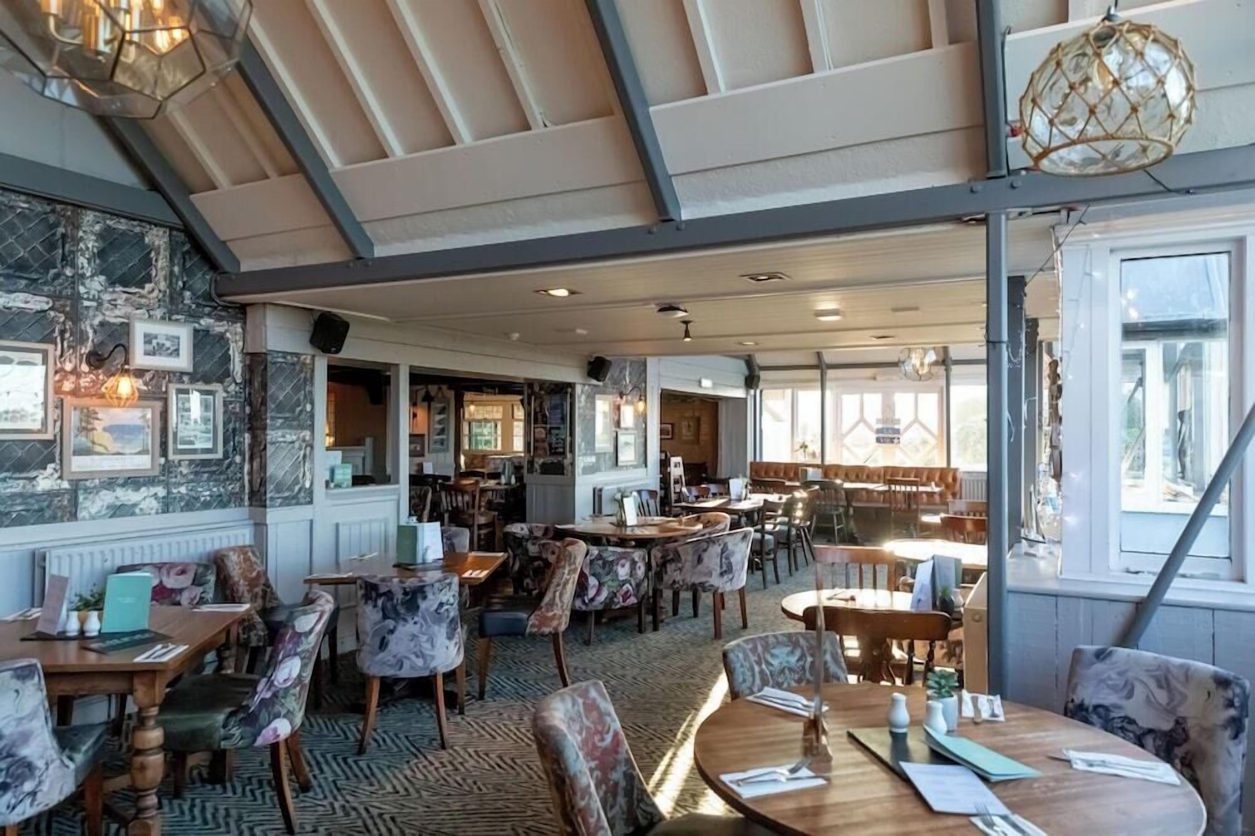 A restaurant with multiple dining tables and chairs, a bar area, and framed pictures on the walls.