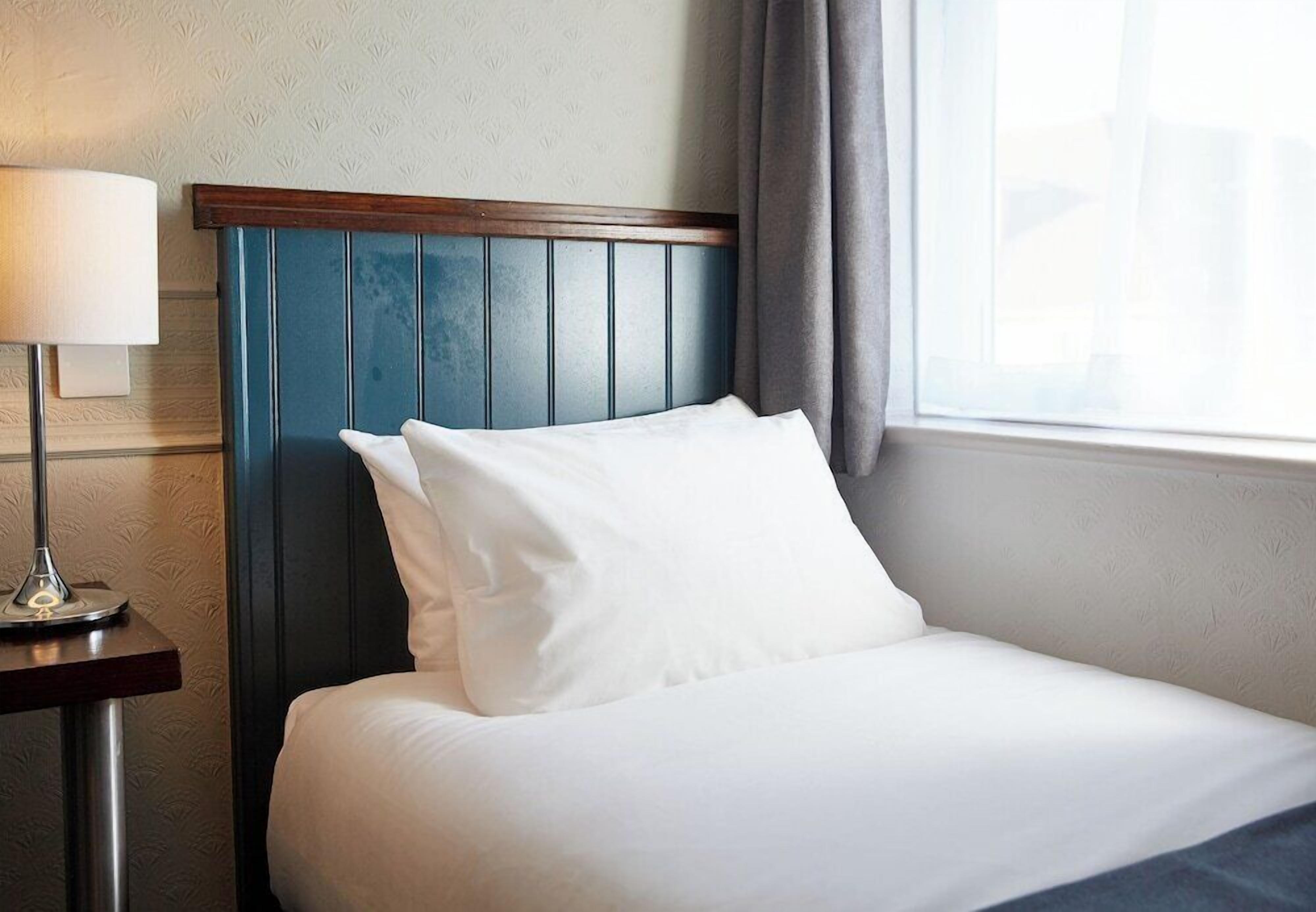 A neatly made bed with white linens, a blue headboard, and a bedside lamp.