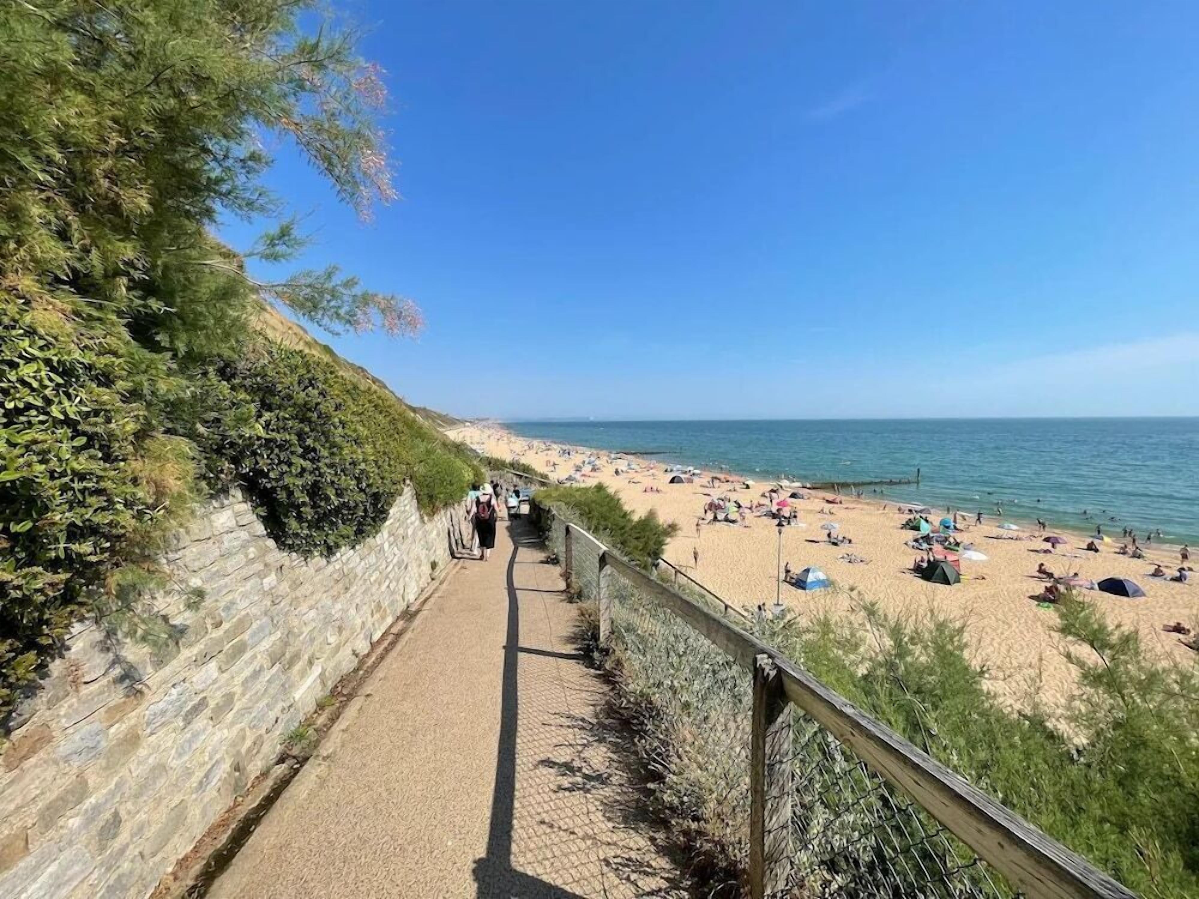 A coastal walkway leading to a sandy beach with clear skies.