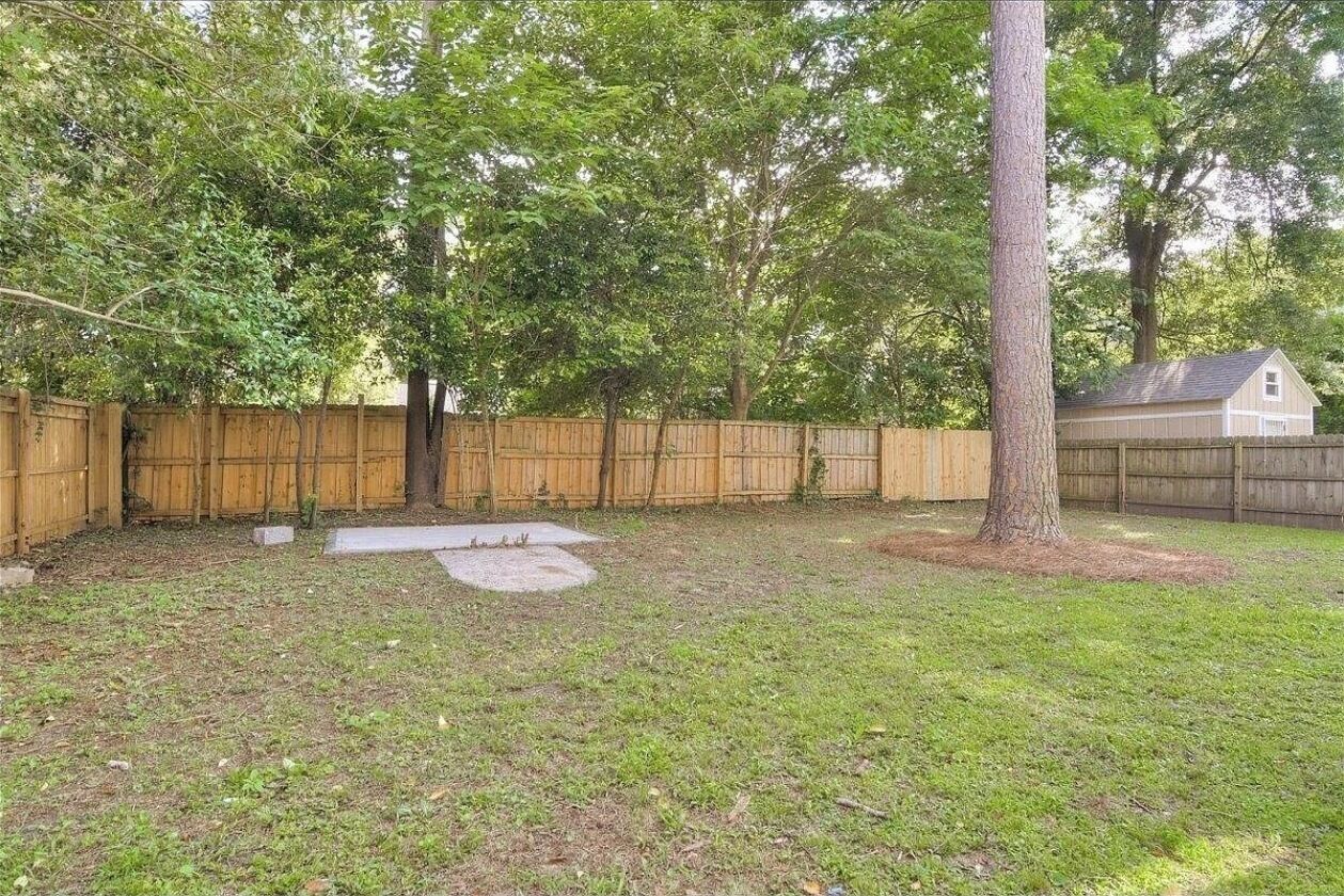 A backyard with a wooden fence, a tree, and a house in the background.