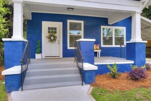 Una casa con fachada azul, detalles blancos, una puerta principal adornada con un adorno navideño, dos ventanas y un porche pequeño con escalones.