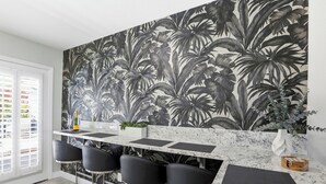 Una cocina con un papel tapiz de hojas tropicales grandes, una encimera de mármol y taburetes negros.