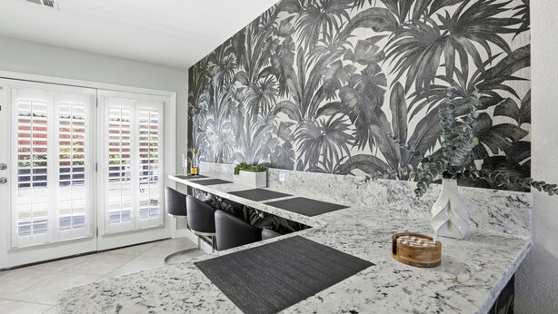Una cocina con un amplio mural de hojas tropicales, encimera de mármol y vistas a través de un ventanal.
