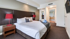 Hotellihuone, jossa on suuri sänky, kaksi yöpöytää valaisimineen, peili ja kylpyhuone, joka näkyy avoimesta ovesta.
