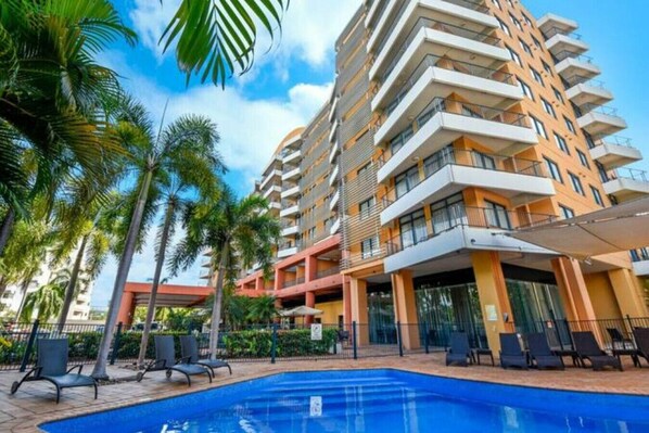 A hotel with a swimming pool, palm trees, and a multi-story building with balconies. - Resort Style City View w/ King Bed, Pool, Balcony (Darwin City)