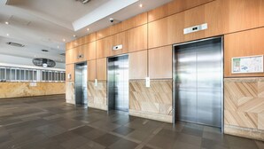 Un espace moderne abritant trois ascenseurs, avec des panneaux muraux en marbre et un comptoir d’accueil.