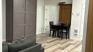 Ein modernes Wohnzimmer mit einem grauen Sofa, einem dunklen Holzschrank und einem Essbereich mit Tisch und Stühlen.