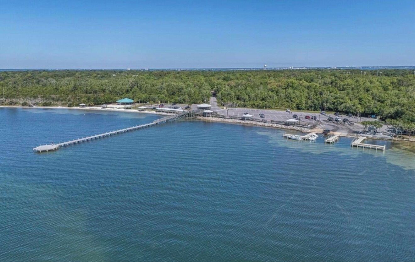 A coastal area with a pier extending into the water, a parking lot, and a building with a green roof.