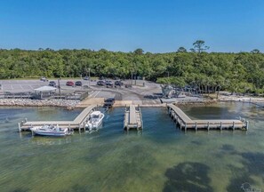 Un puerto deportivo con barcos amarrados, una zona de estacionamiento y un fondo arbolado.