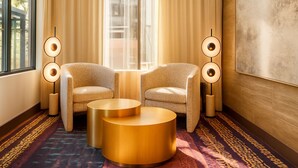 Una habitación con dos sillones, una mesa redonda dorada y lámparas de pie.