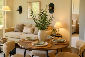 A living room with a sofa, a coffee table with placemats and plates, a potted plant, wall-mounted lamps, and a mirror. - Chevy Chase  315  2BR (Chevy Chase)