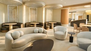 Un moderno vestíbulo de hotel con un sofá curvo, sillones y mesas redondas.