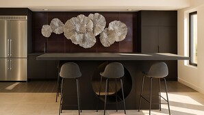 Una cocina moderna con una isla central, tres taburetes de bar y un elemento decorativo en la pared.