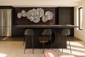 A modern kitchen with a central island, three bar stools, and a decorative wall piece. - Chevy Chase  315  2BR (Chevy Chase)