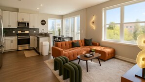 A modern kitchen with stainless steel appliances, a dining area with a sofa and coffee table, and large windows offering a view of the outdoors. - Chevy Chase 414 3BR (Chevy Chase)