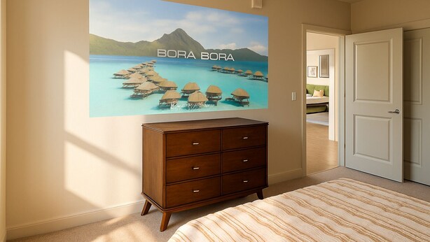 A bedroom with a bed, a dresser, and a wall-mounted TV displaying a tropical beach scene. - Chevy Chase 414 3BR (Chevy Chase)