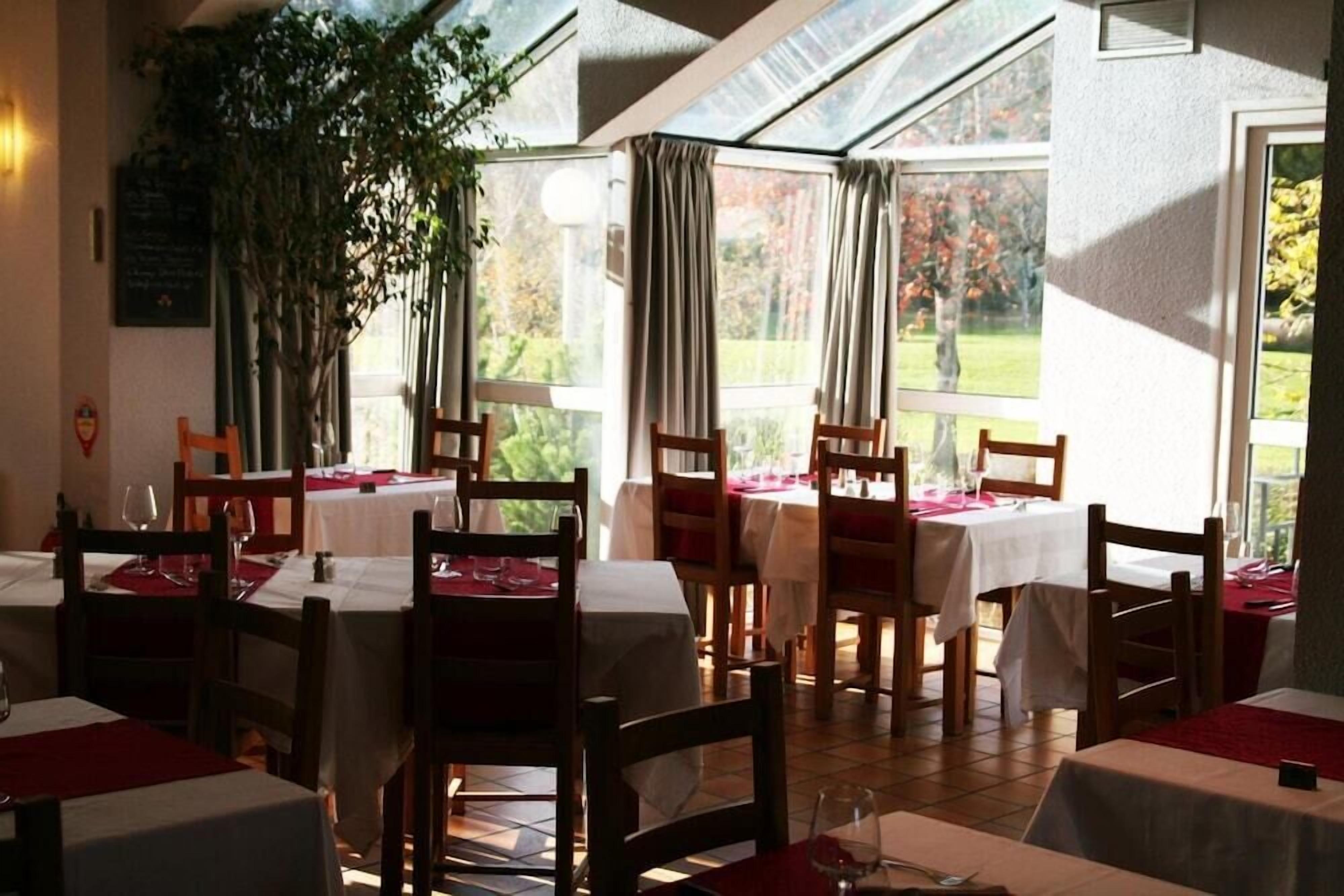 Un restaurante con varias mesas y sillas, grandes ventanales y vistas al exterior.