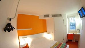 Um quarto com uma cama, uma escrivaninha, uma televisão e uma janela.
