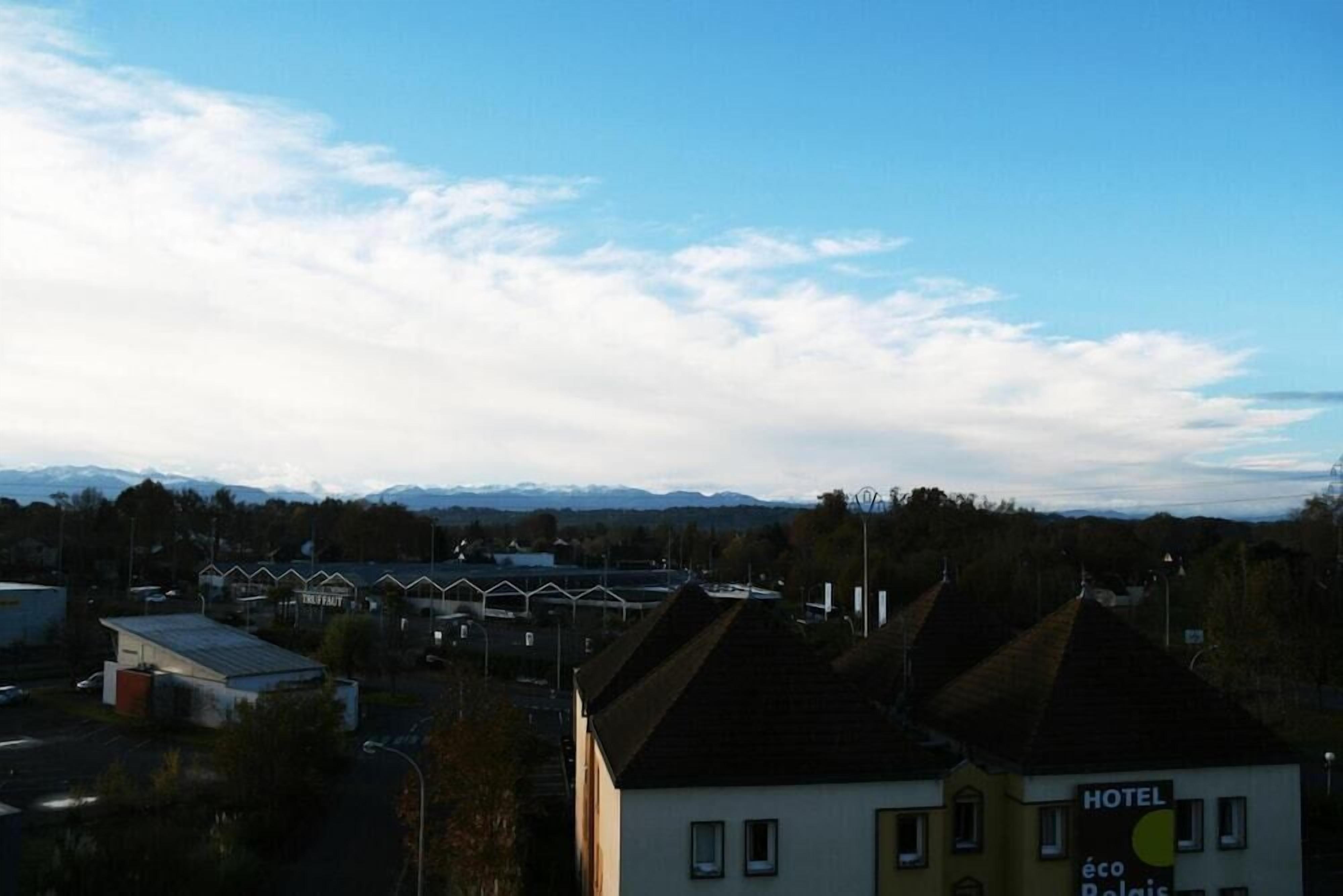 Un hotel con un cartello che indica 'HOTEL éco Relais' e vista su una città con edifici e montagne sullo sfondo.