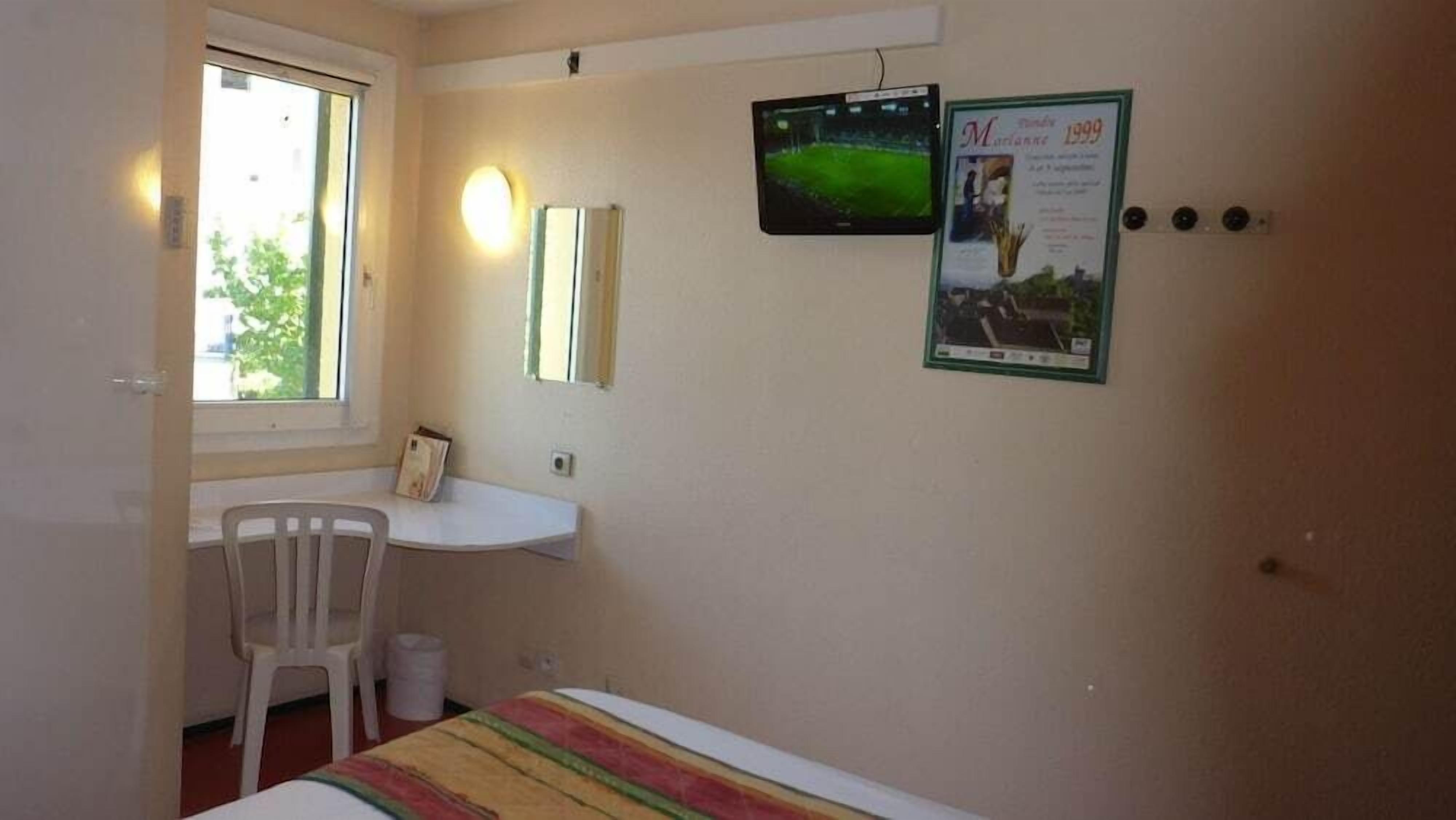 Una habitación pequeña con una cama, un escritorio, una silla, un ventanal y dos objetos enmarcados en la pared.