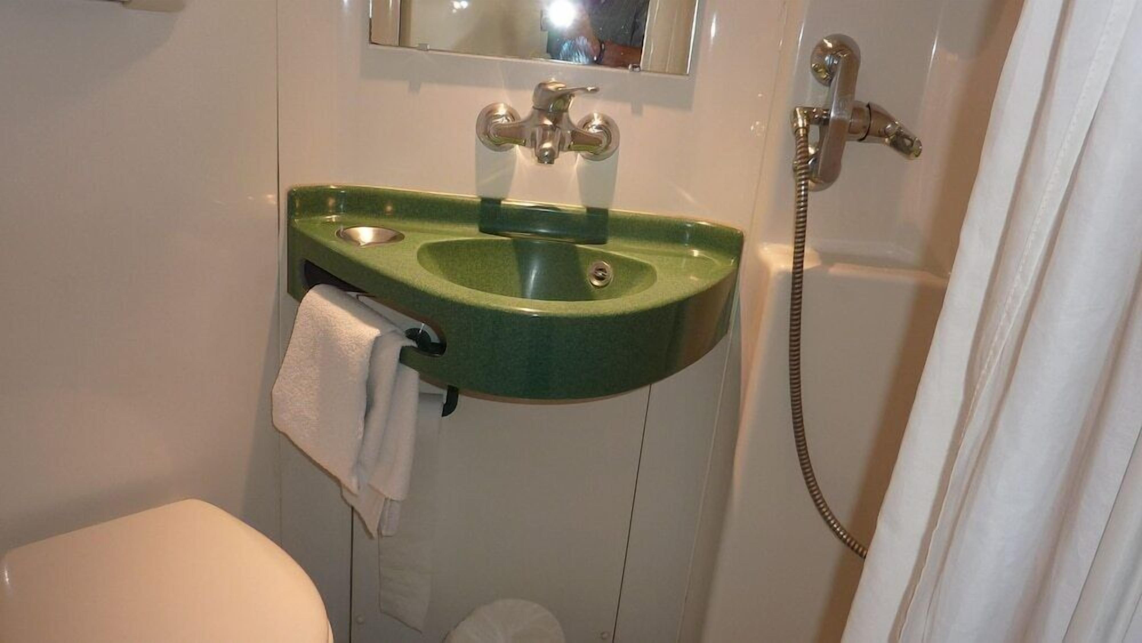 Un baño con un lavabo verde, un espejo, un inodoro y una cortina de ducha.