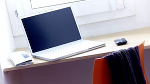 Um laptop sobre uma mesa com um caderno, um telemóvel e uma cadeira.