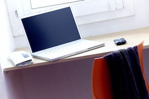 Un ordinateur portable sur un bureau, avec un carnet, un tél éphone portable et une chaise.