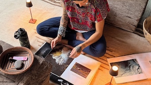 Une personne assise sur un plancher en bois, avec un livre, une lampe et une bouteille d’eau.