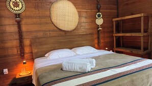Une pièce en bois avec un lit, un objet tissé suspendu au mur et une étagère.