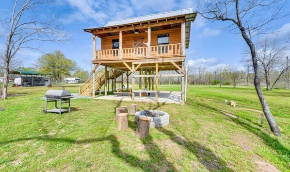 Una cabaña de madera con balcón, una parrilla y una chimenea en un área con césped.